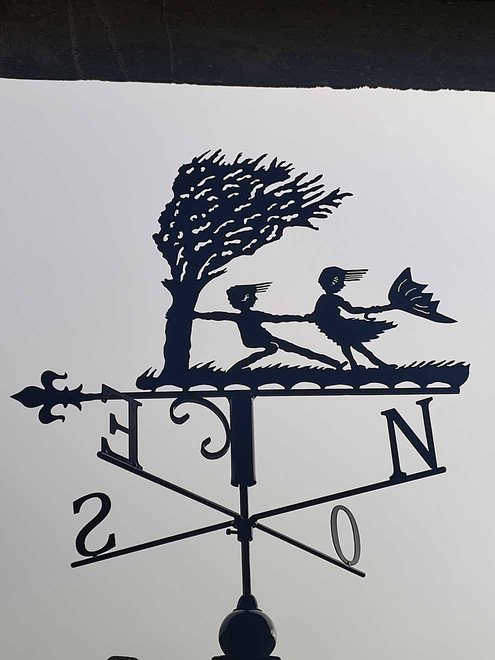 Une girouette représentant deux enfants qui s'accrochent à un arbre pour ne pas être emportés par le vent